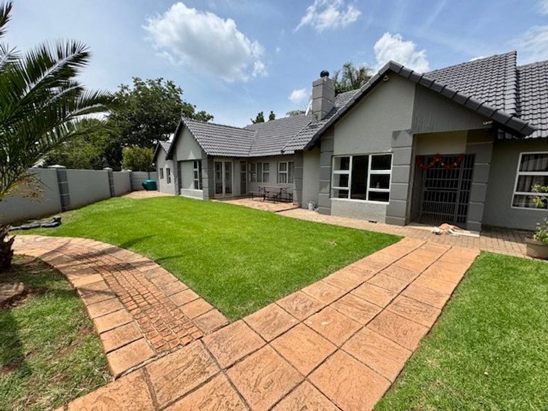 Rear view of the house featuring a well-maintained lawn, paved walkways, a patio area, and a secure perimeter wall.