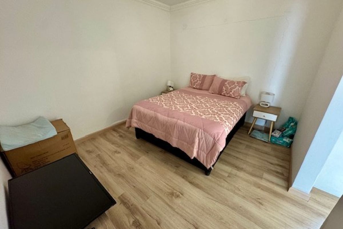 A bedroom featuring light wood-look laminate flooring and coving, currently showing visible cracks on the wall surface.