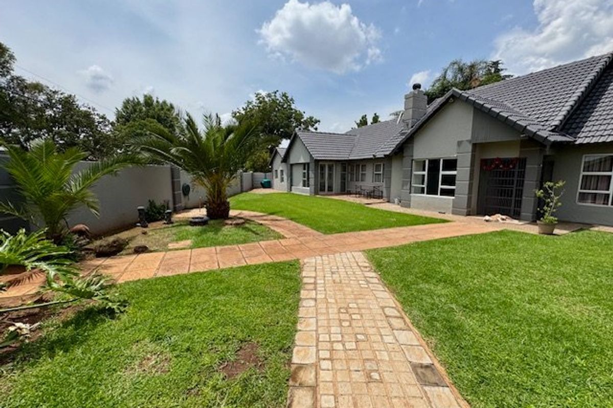 A well-maintained rear garden featuring a paved walkway, manicured lawn, and a spacious exterior facade with a tiled roof.