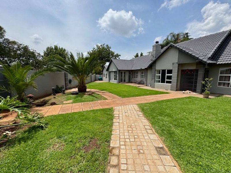 A well-maintained rear garden featuring a paved walkway, manicured lawn, and a spacious exterior facade with a tiled roof.