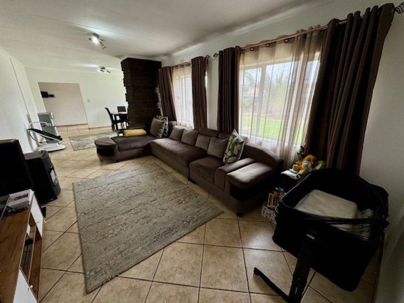 Spacious open-plan living area featuring tiled flooring, a prominent brick fireplace, and large windows allowing for natural light.