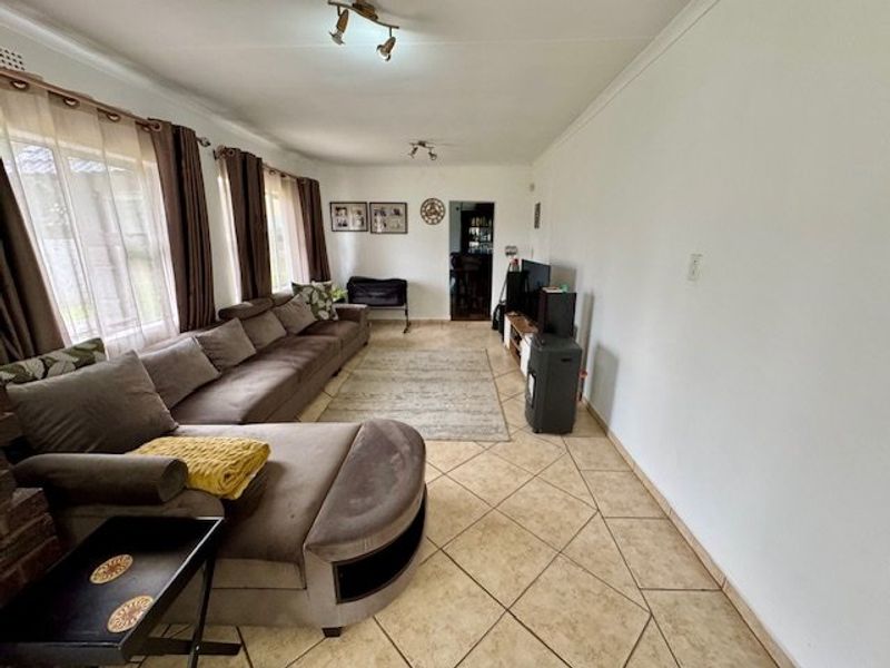 A spacious living room featuring neutral ceramic floor tiles, coved ceilings, and large windows allowing for natural light.
