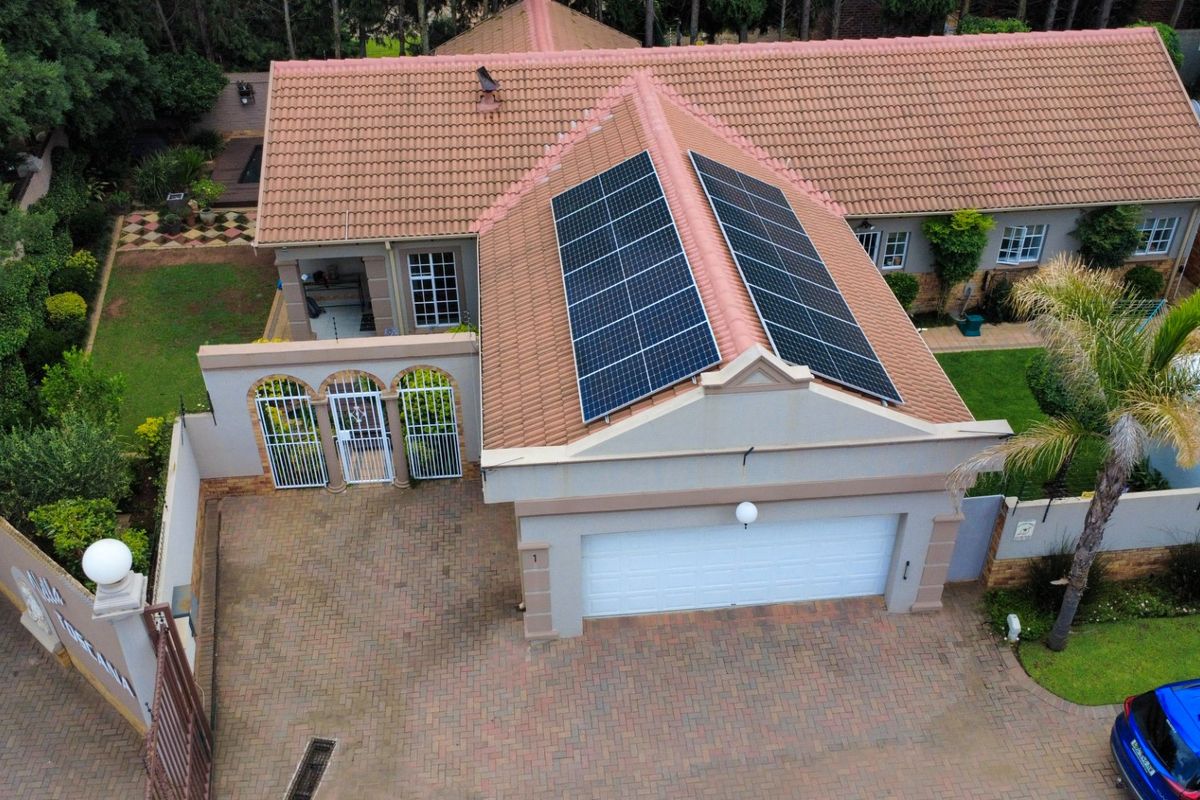 Aerial view of a townhouse featuring a tiled roof with installed solar panels, a paved driveway, and a secure double garage entrance.
