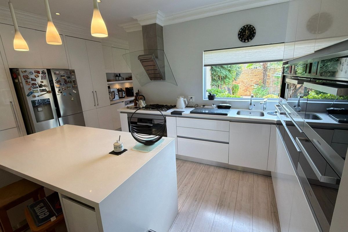 Modern kitchen featuring white high-gloss cabinetry, a central island with quartz countertops, integrated appliances, and a gas hob with a glass extractor fan.