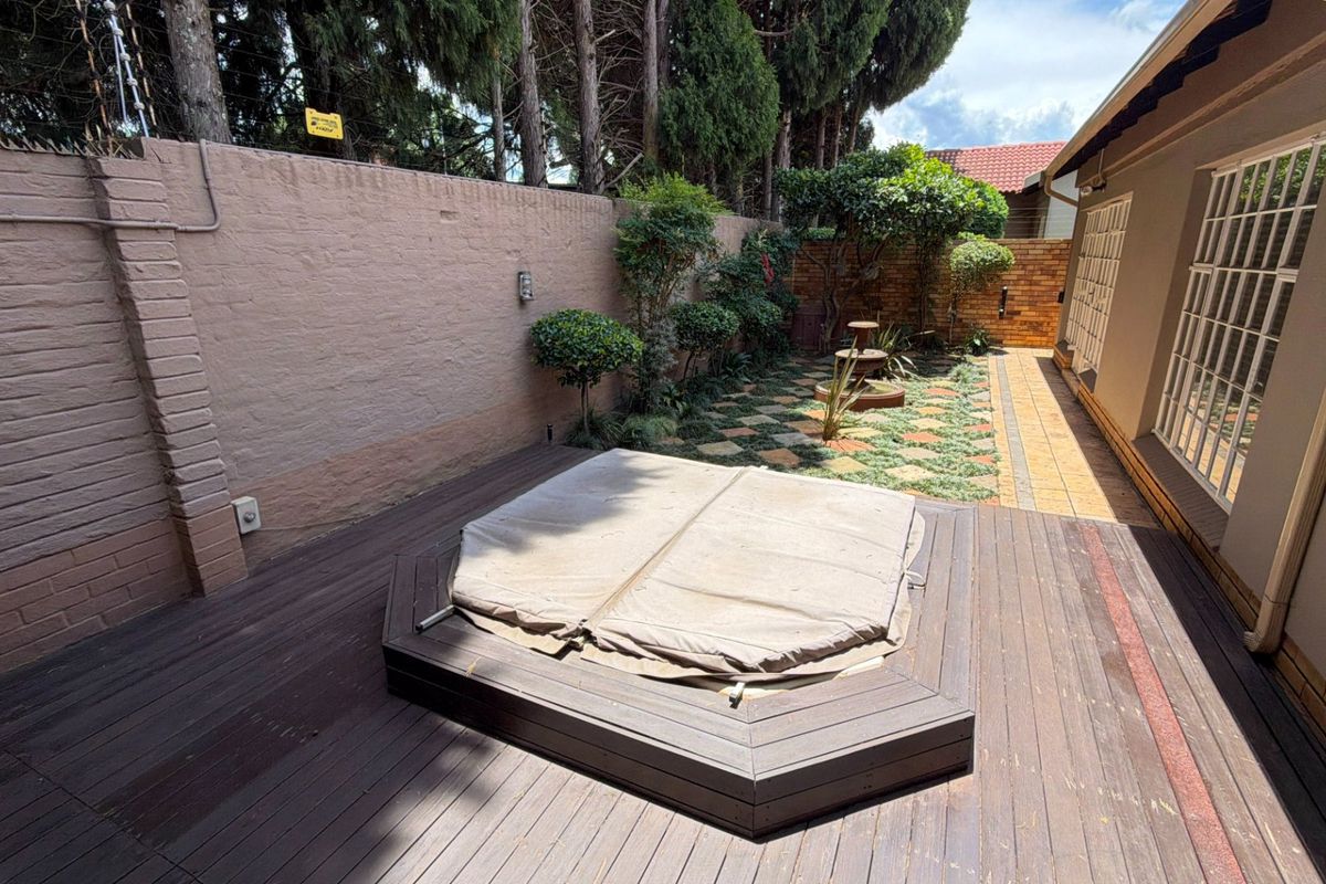 Rear courtyard featuring a timber deck with a built-in spa, paved pathways, and a secure brick boundary wall.
