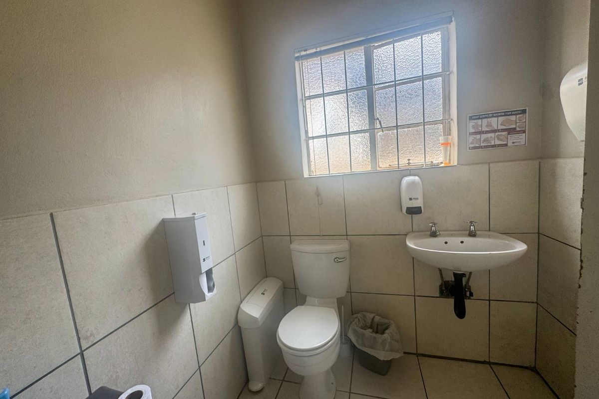 A functional commercial restroom featuring tiled walls and flooring, a wall-mounted washbasin, and a standard toilet with integrated soap dispenser.