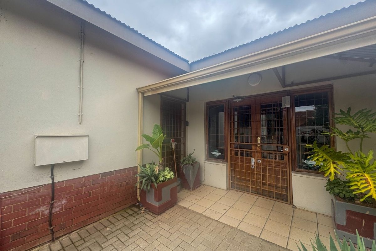 A paved rear courtyard area featuring a covered patio entrance with security gates and brick and plaster wall finishes.