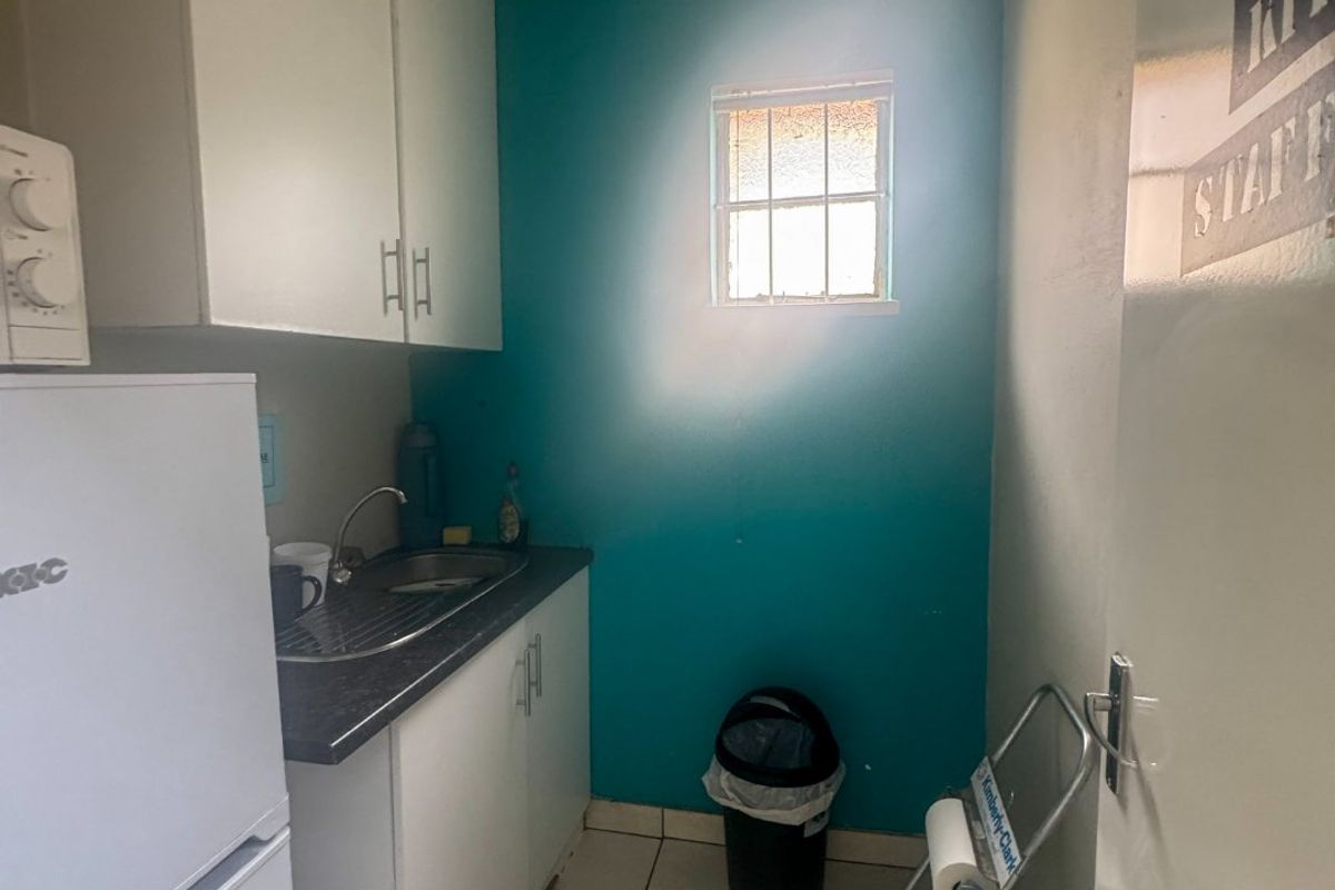 A compact staff kitchen area featuring built-in white cabinetry, a laminate countertop with a stainless steel sink, and tiled flooring.