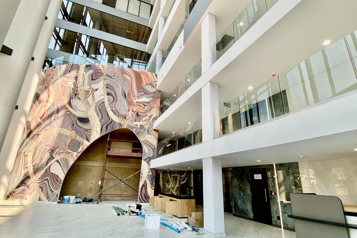 Spacious commercial atrium entrance featuring a multi-level design, glass balustrades, and a striking decorative feature wall under construction.