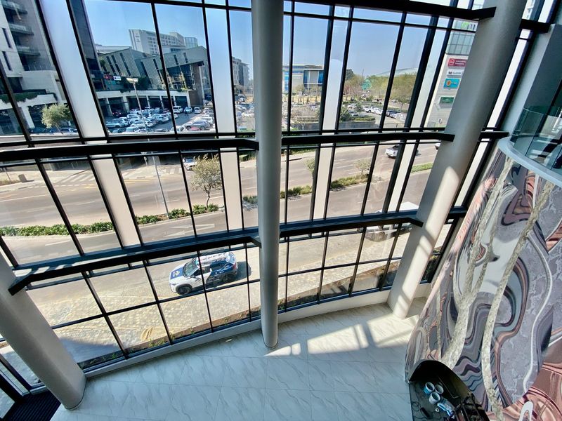 High-level view from a modern commercial building featuring expansive floor-to-ceiling windows overlooking the street and surrounding urban landscape.