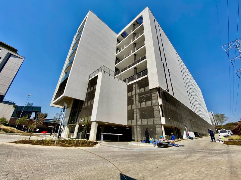 Modern multi-story commercial building featuring a clean white facade, integrated balconies, and secure ground-level parking access with a paved driveway.