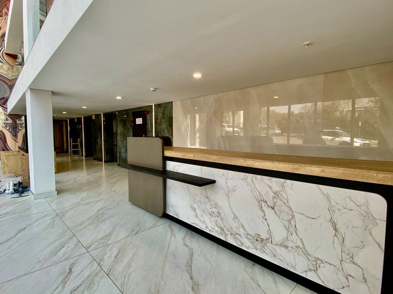 Modern commercial lobby featuring a sleek built-in reception desk, high-end marble-look floor and wall finishes, and recessed lighting.