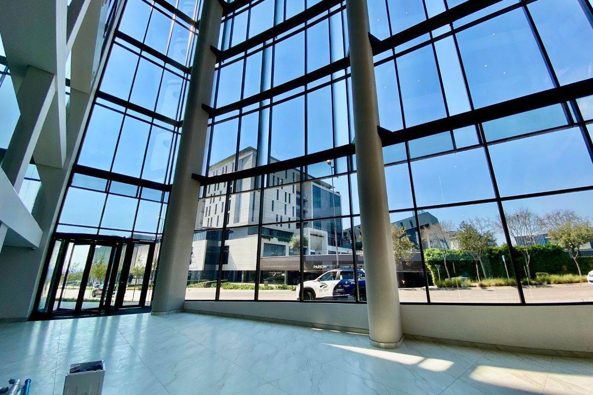 Spacious commercial entrance lobby featuring floor-to-ceiling glass curtain walls, structural columns, and polished marble-look flooring with abundant natural light.