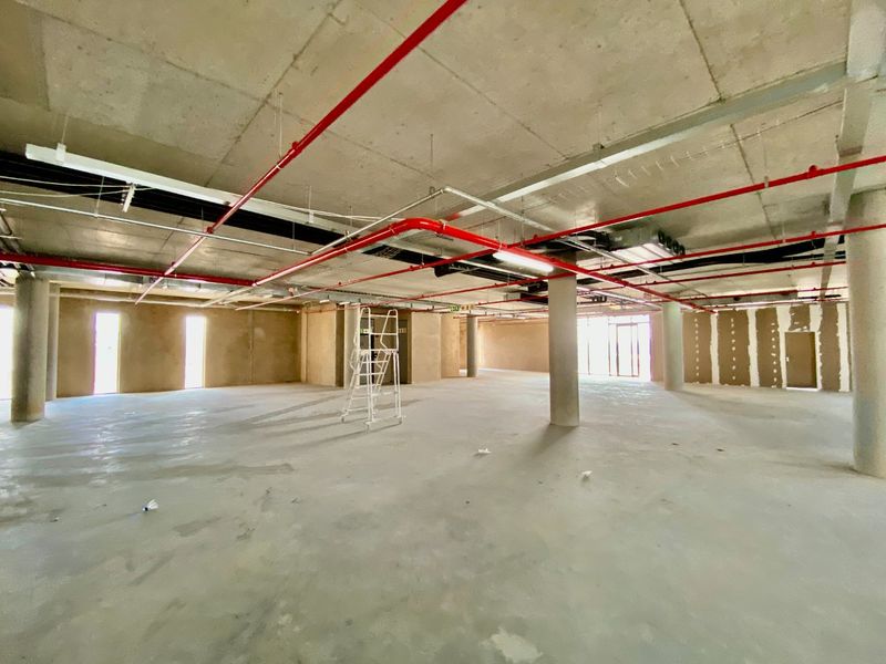 A large, open-plan commercial space in shell condition featuring exposed concrete ceilings, fire sprinkler systems, and concrete flooring, ready for custom fit-out.