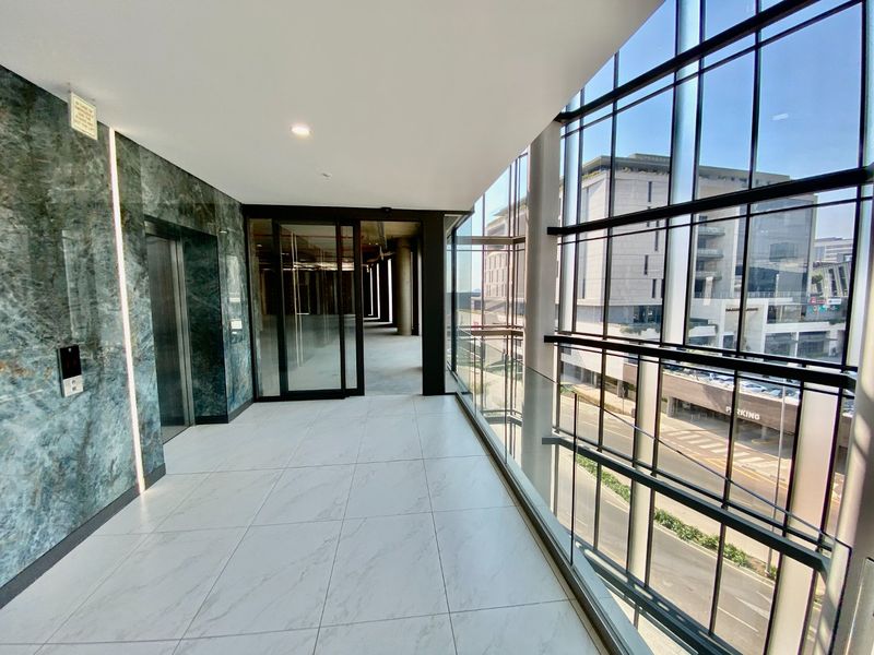 Modern commercial hallway featuring large format floor tiles, a marble-clad feature wall, and expansive floor-to-ceiling glass windows overlooking the street.