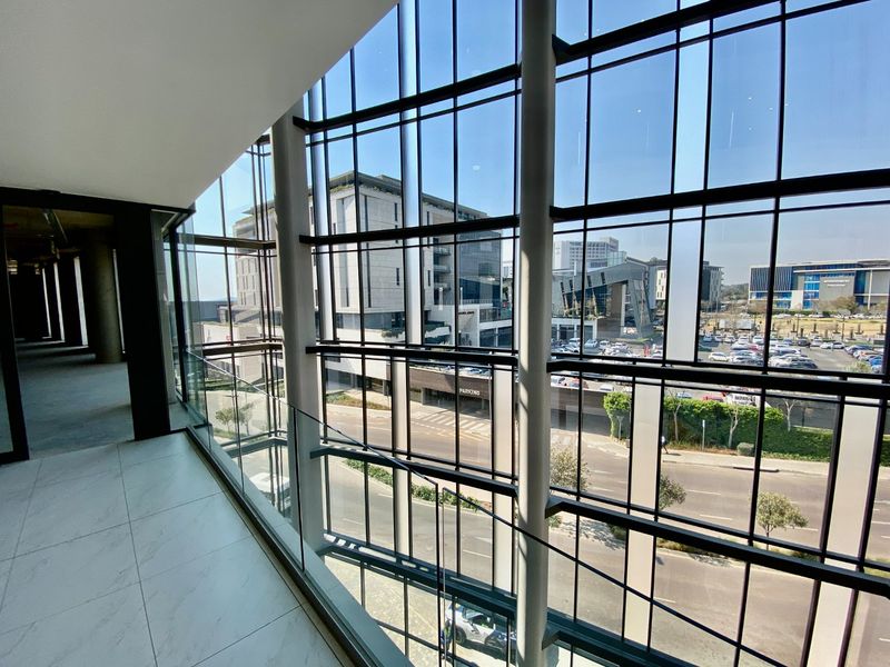 Modern commercial hallway featuring expansive floor-to-ceiling windows with views of the surrounding business district and street level.