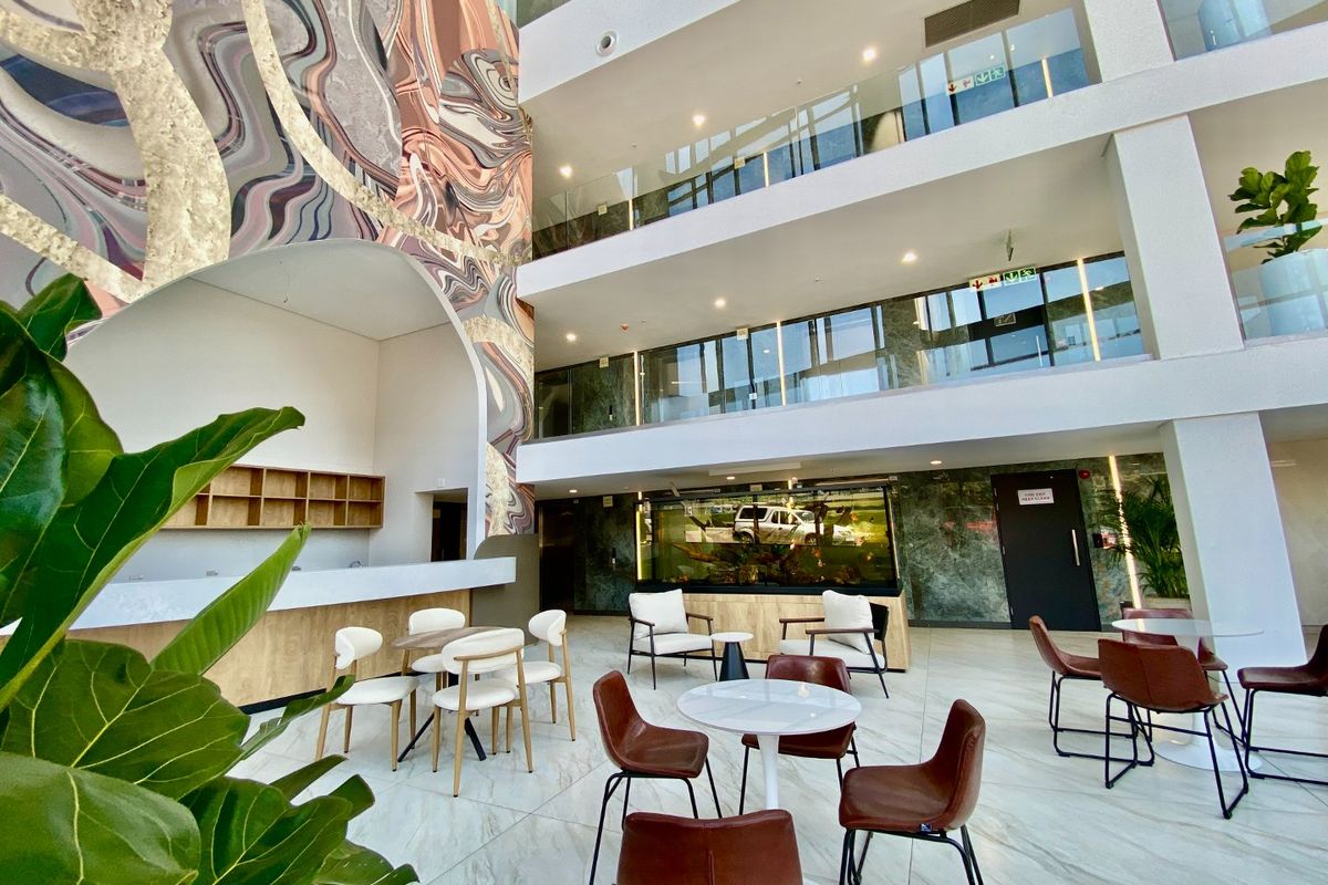 Spacious commercial atrium featuring a multi-level design, glass balustrades, marble-look flooring, and a striking feature wall mural in a modern, well-maintained lobby area.