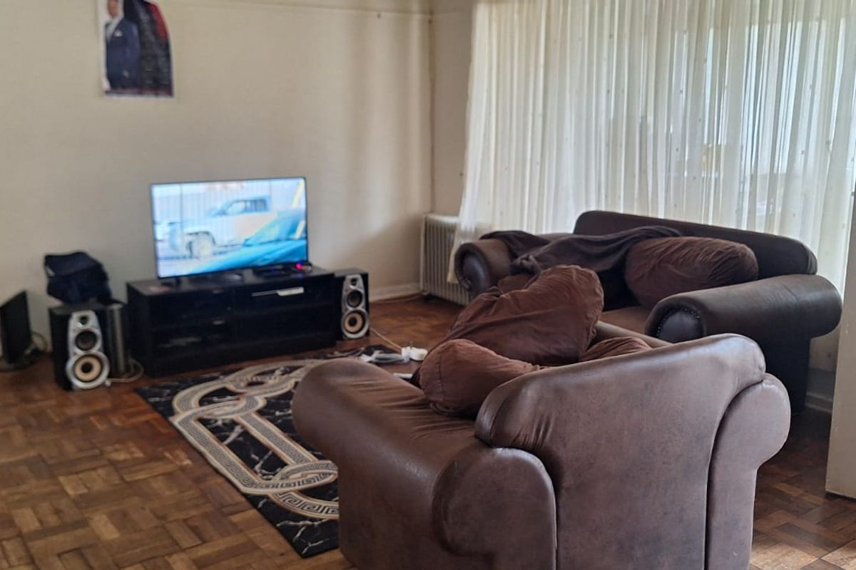 A living room featuring original parquet flooring, large windows with curtains, and a radiator heating unit.