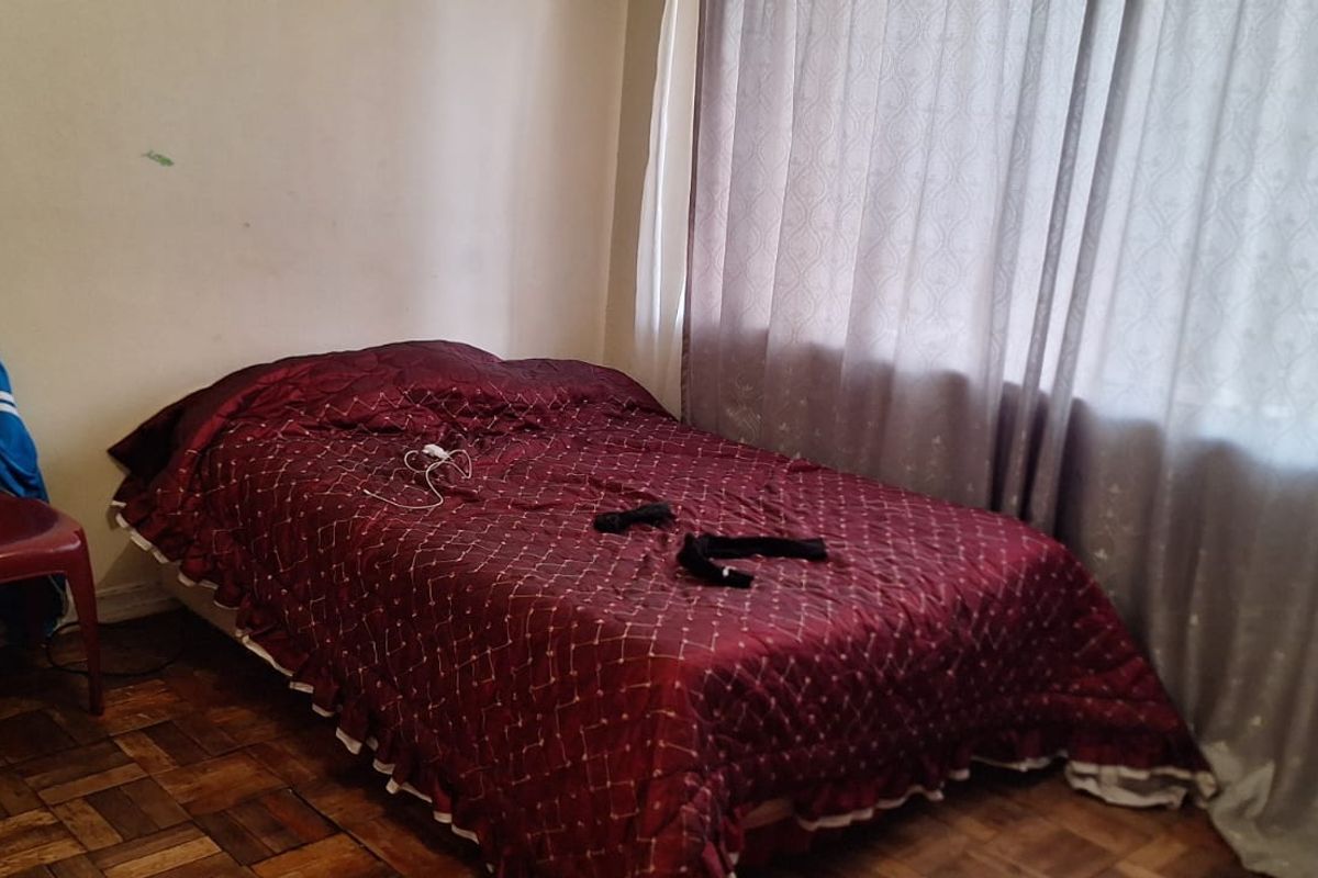 A bedroom featuring parquet flooring and large window with curtains.
