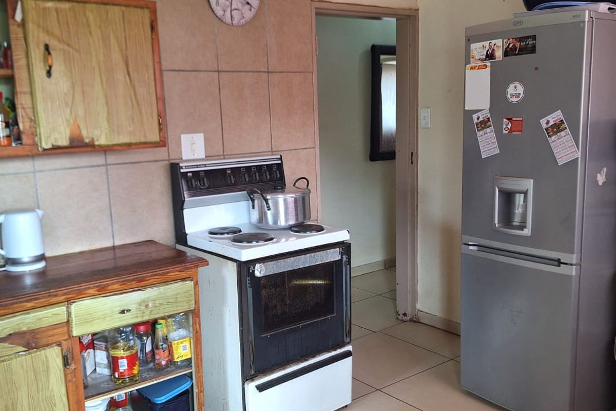 A functional kitchen featuring tiled walls, built-in wooden cabinetry, and a freestanding electric stove.