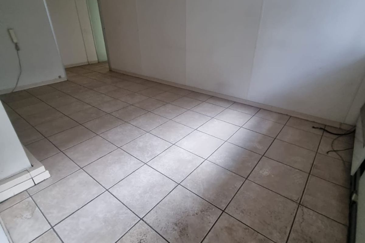 An empty commercial office space featuring tiled flooring and recessed fluorescent lighting, suitable for various business configurations.