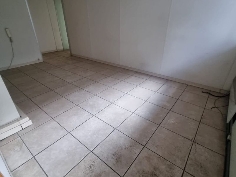 An empty commercial office space featuring tiled flooring and recessed fluorescent lighting, suitable for various business configurations.