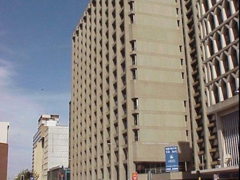A multi-story commercial office building featuring a concrete facade with recessed window detailing, situated in a busy urban street environment.