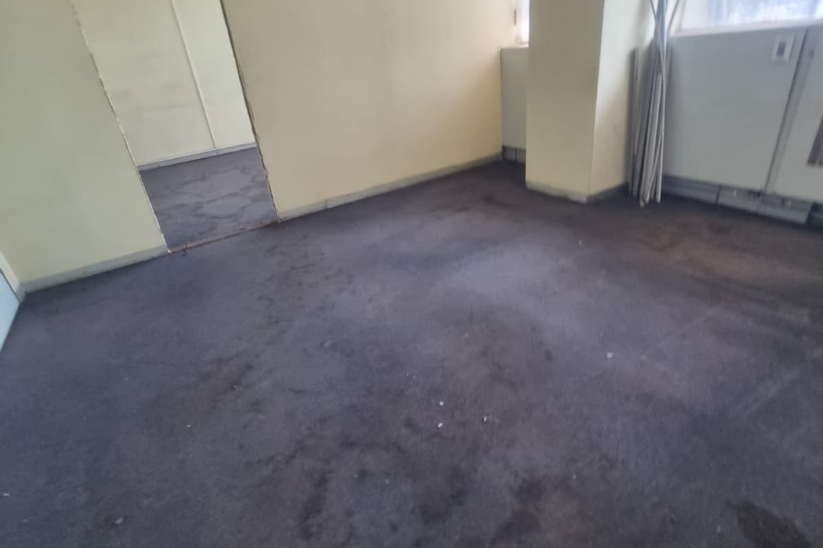 An empty office space featuring worn carpeting, a suspended ceiling, and an unfinished doorway, requiring cosmetic updates and flooring replacement.