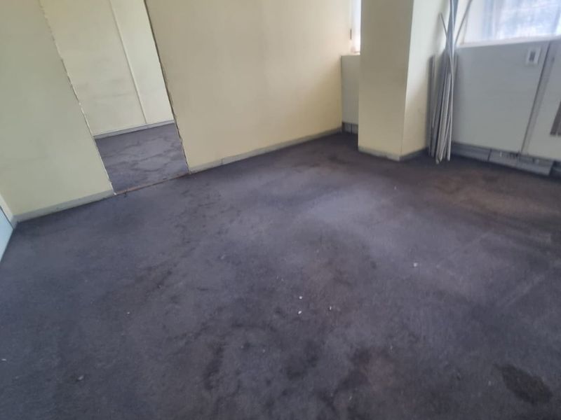 An empty office space featuring worn carpeting, a suspended ceiling, and an unfinished doorway, requiring cosmetic updates and flooring replacement.