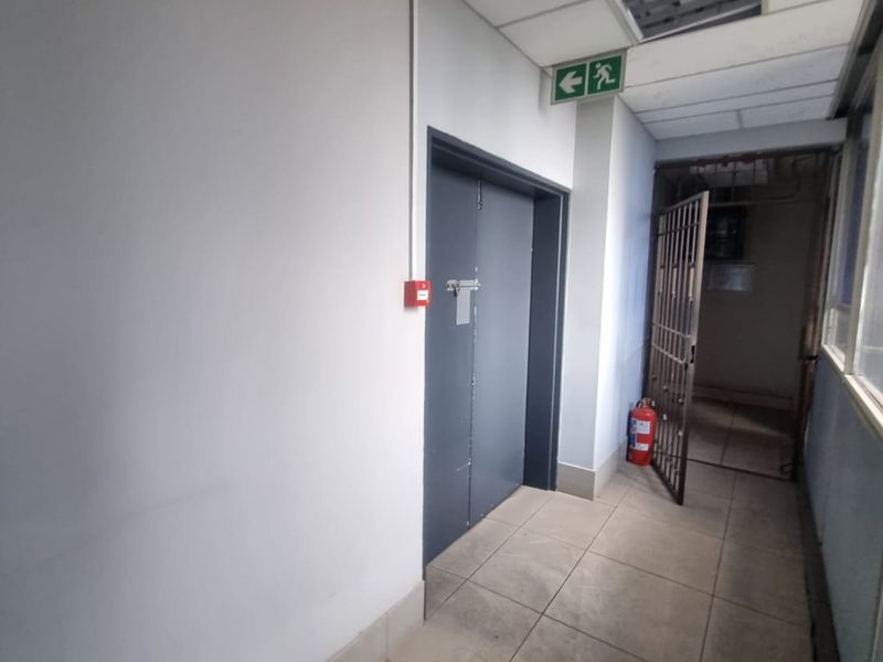 A functional commercial hallway featuring tiled flooring, a suspended ceiling with integrated lighting, and a secure metal gate.