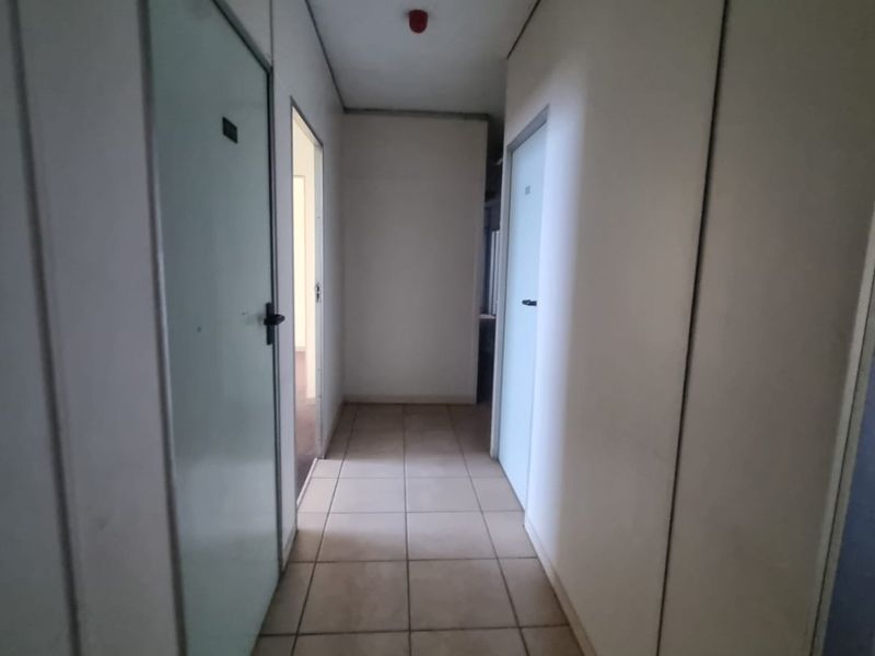 A functional commercial hallway featuring tiled flooring and a suspended ceiling, providing access to multiple office or utility rooms.