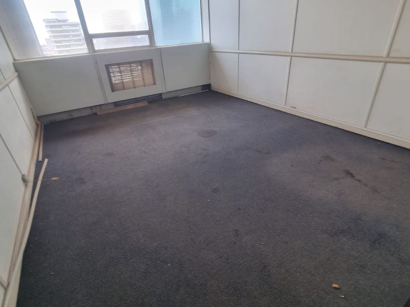 An empty office space featuring partitioned wall panels, carpet flooring, and a built-in HVAC unit, requiring cosmetic updates to improve its professional appeal.