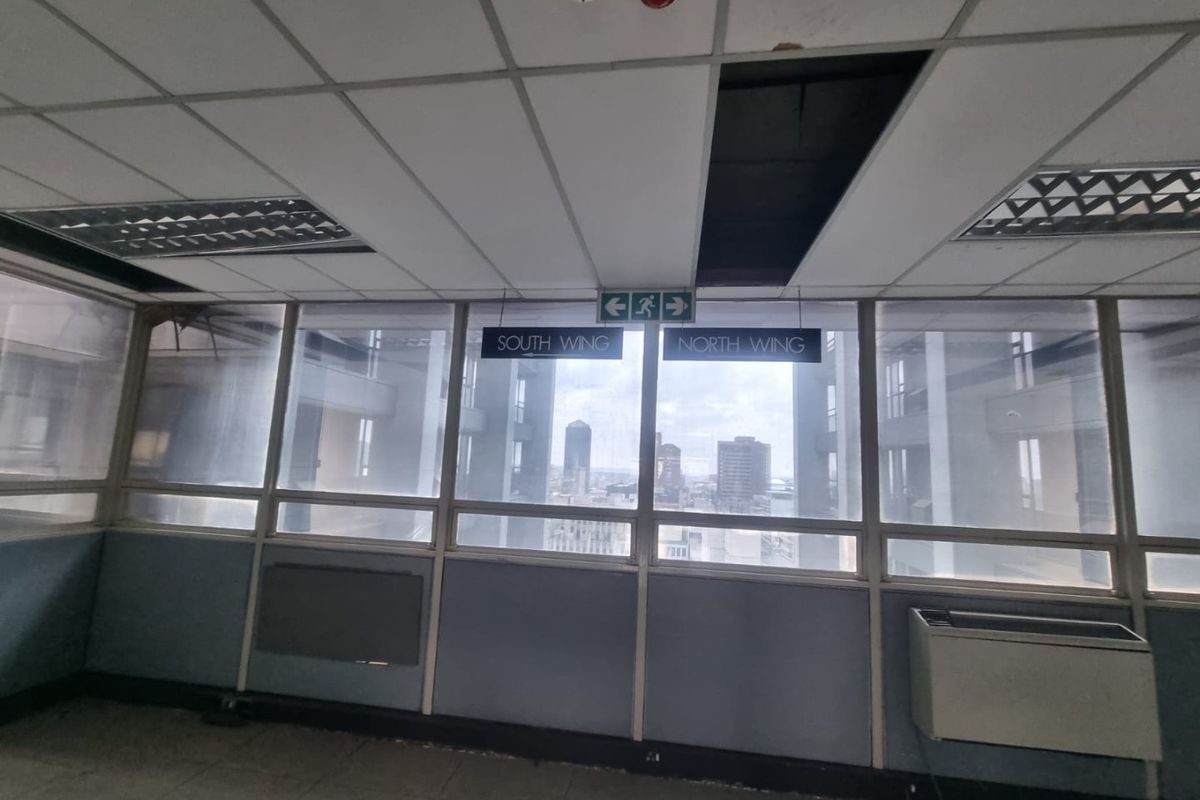Commercial hallway featuring large windows with city views, suspended ceiling, and directional signage. The space requires maintenance and cosmetic updates.