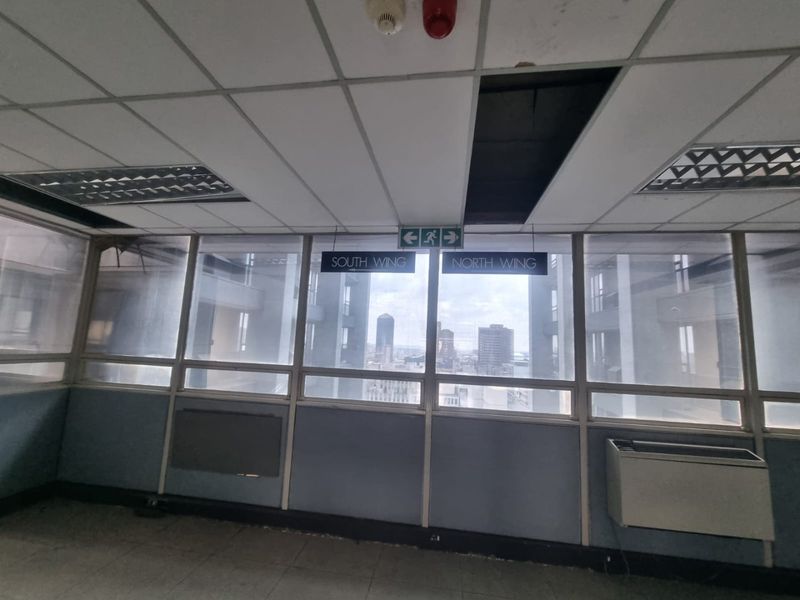 Commercial hallway featuring large windows with city views, suspended ceiling, and directional signage. The space requires maintenance and cosmetic updates.