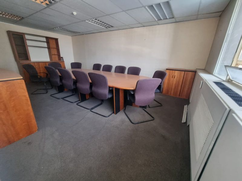 A functional commercial office space featuring a large boardroom table, built-in storage cabinetry, suspended ceiling tiles, and carpeted flooring.