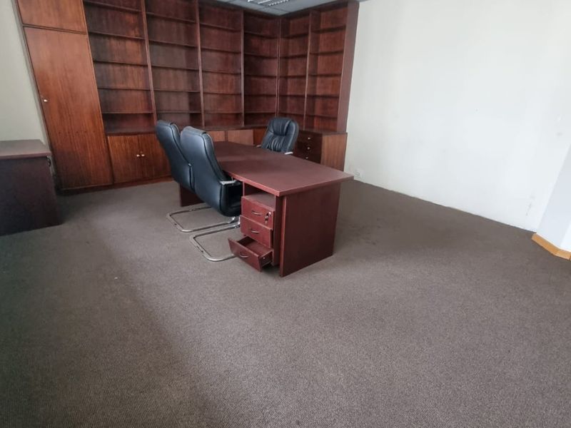 A commercial office space featuring extensive built-in wooden shelving, suspended ceiling tiles, and carpeted flooring.