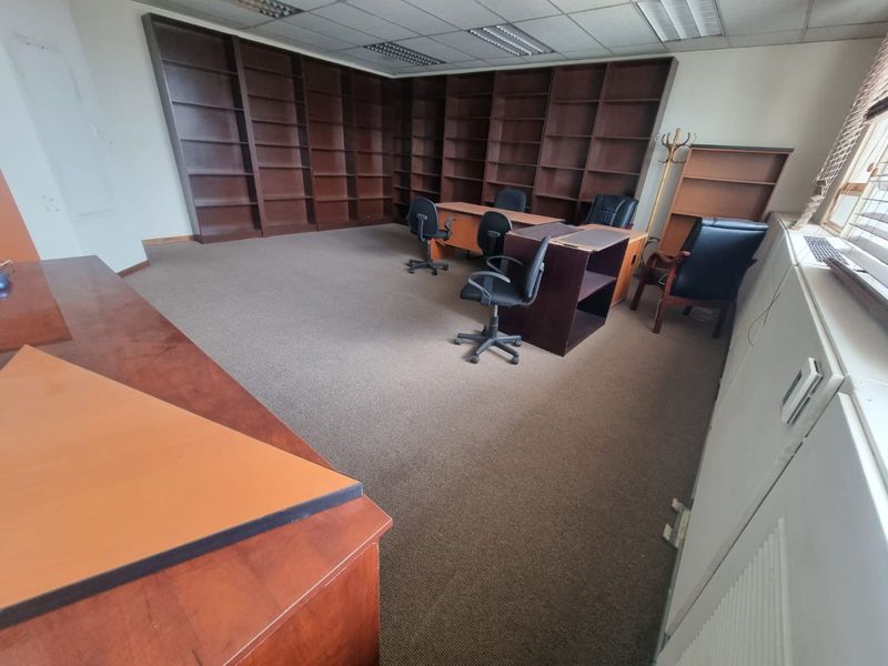 Spacious commercial office featuring extensive built-in wooden shelving, carpeted flooring, and a suspended ceiling with integrated lighting.