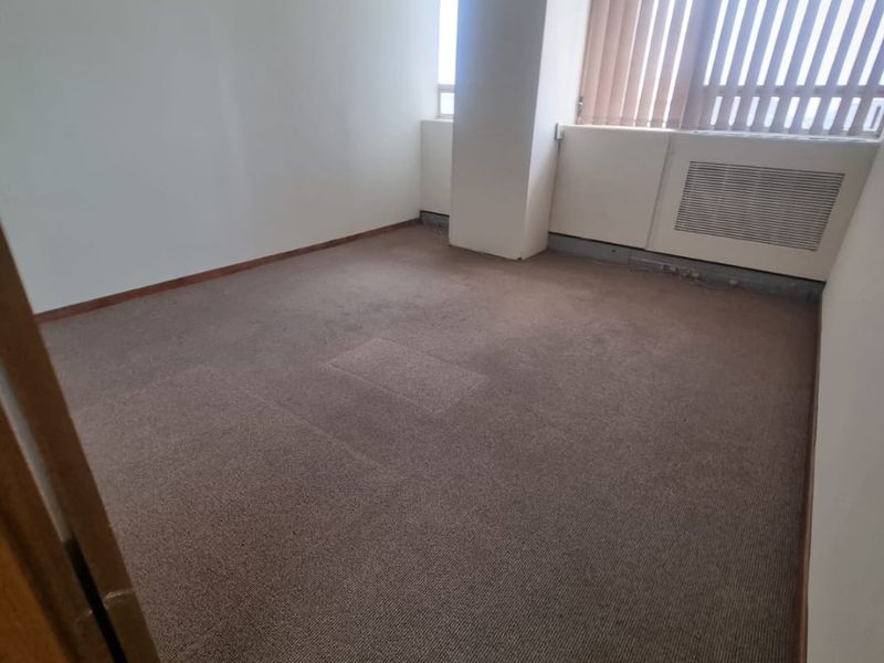 An empty commercial office space featuring carpeted flooring, a suspended ceiling, and vertical window blinds.