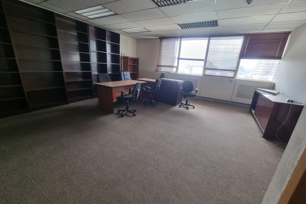 Spacious commercial office featuring built-in floor-to-ceiling shelving, suspended ceiling with recessed lighting, and large windows with venetian blinds.