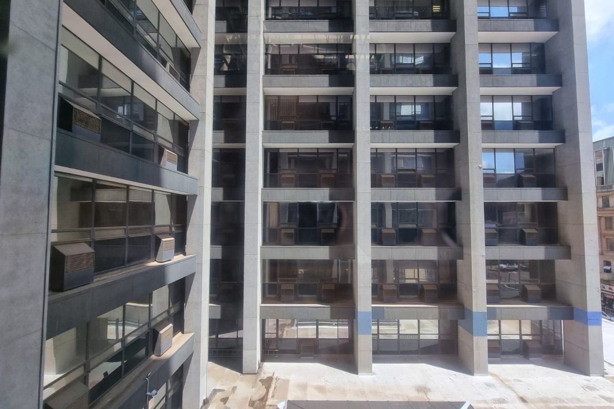 Exterior view of a multi-story commercial building facade featuring concrete structure, tinted windows, and integrated air conditioning units overlooking a paved courtyard.