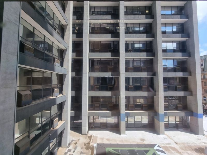 Exterior view of a multi-story commercial building facade featuring concrete structure, tinted windows, and integrated air conditioning units overlooking a paved courtyard.