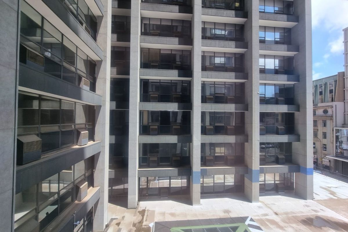 Exterior view of a multi-story commercial building featuring a concrete facade, large glass windows, and a paved courtyard area.