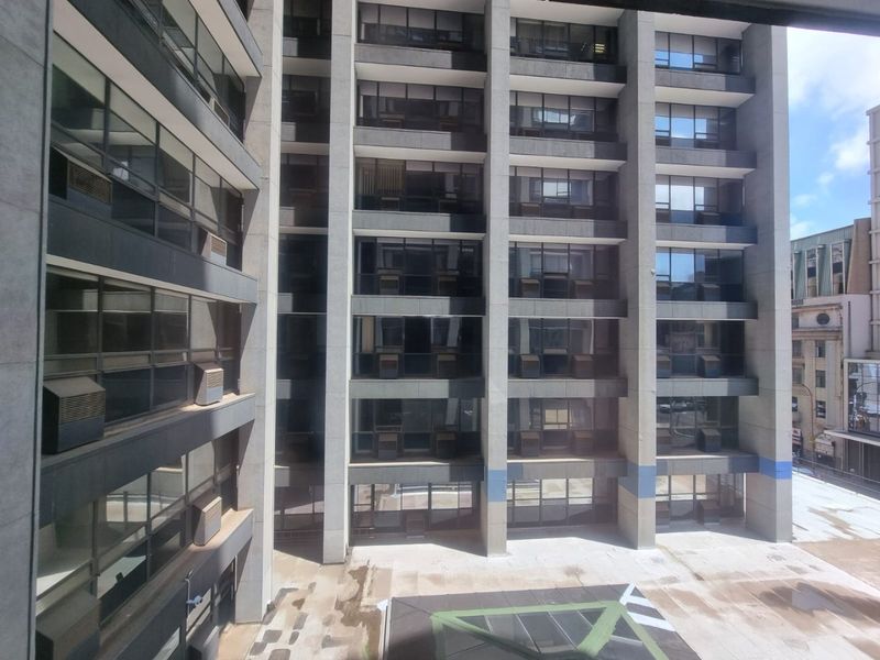 Exterior view of a multi-story commercial building featuring a concrete facade, large glass windows, and a paved courtyard area.