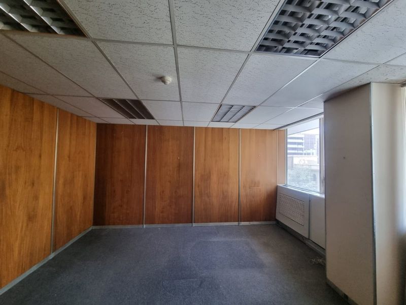 An empty commercial office space featuring wood veneer wall paneling, a suspended ceiling with recessed lighting, and carpet flooring.