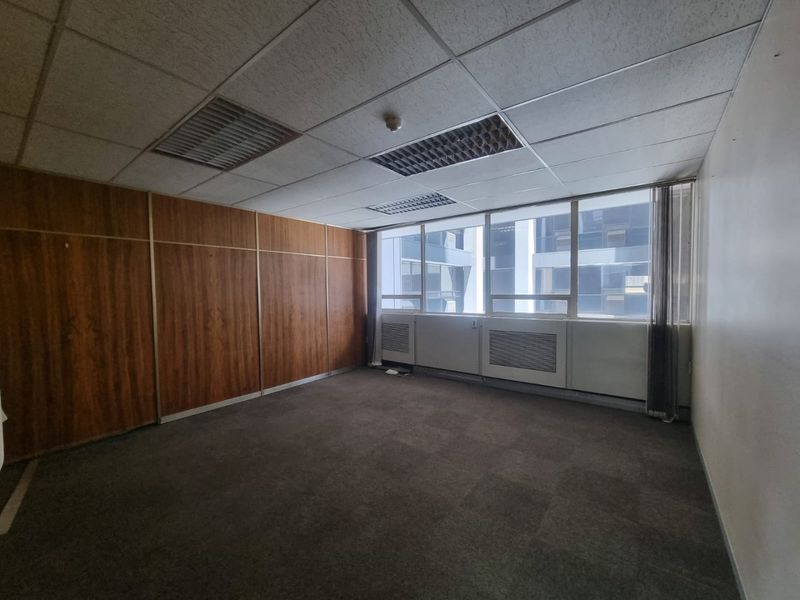 Empty commercial office space featuring wood paneling, suspended ceiling with recessed lighting, and large windows providing natural light.