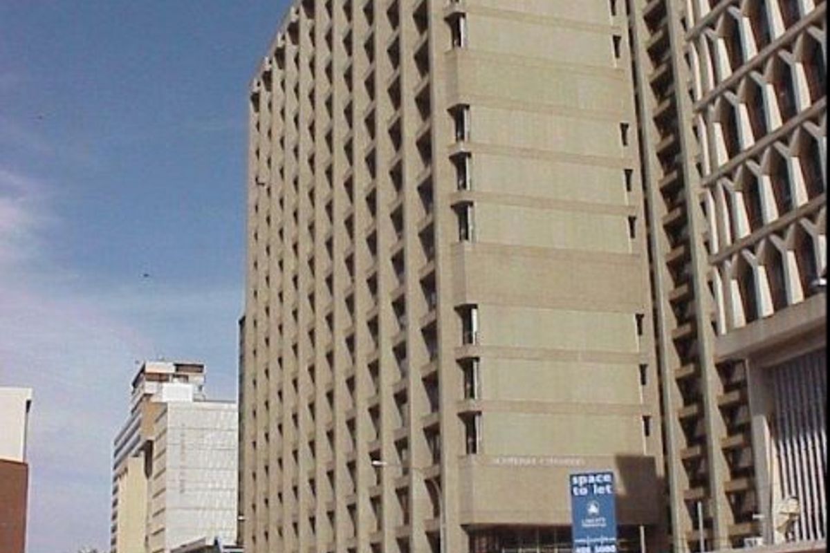 A multi-story commercial office building featuring a concrete facade with recessed window detailing, situated in a busy urban street environment.