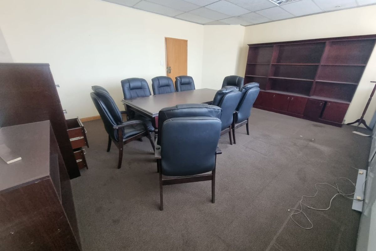 A functional office space featuring a suspended ceiling, recessed lighting, built-in shelving, and carpeted flooring, suitable for a professional meeting or workspace environment.