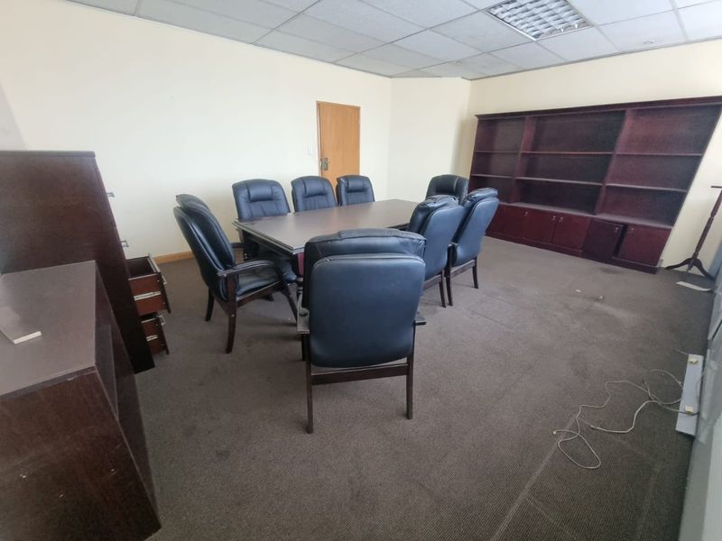 A functional office space featuring a suspended ceiling, recessed lighting, built-in shelving, and carpeted flooring, suitable for a professional meeting or workspace environment.