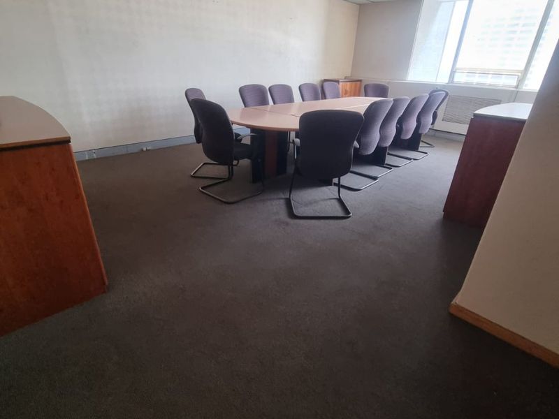 A functional office meeting room featuring a suspended ceiling, recessed lighting, and large windows providing natural light.