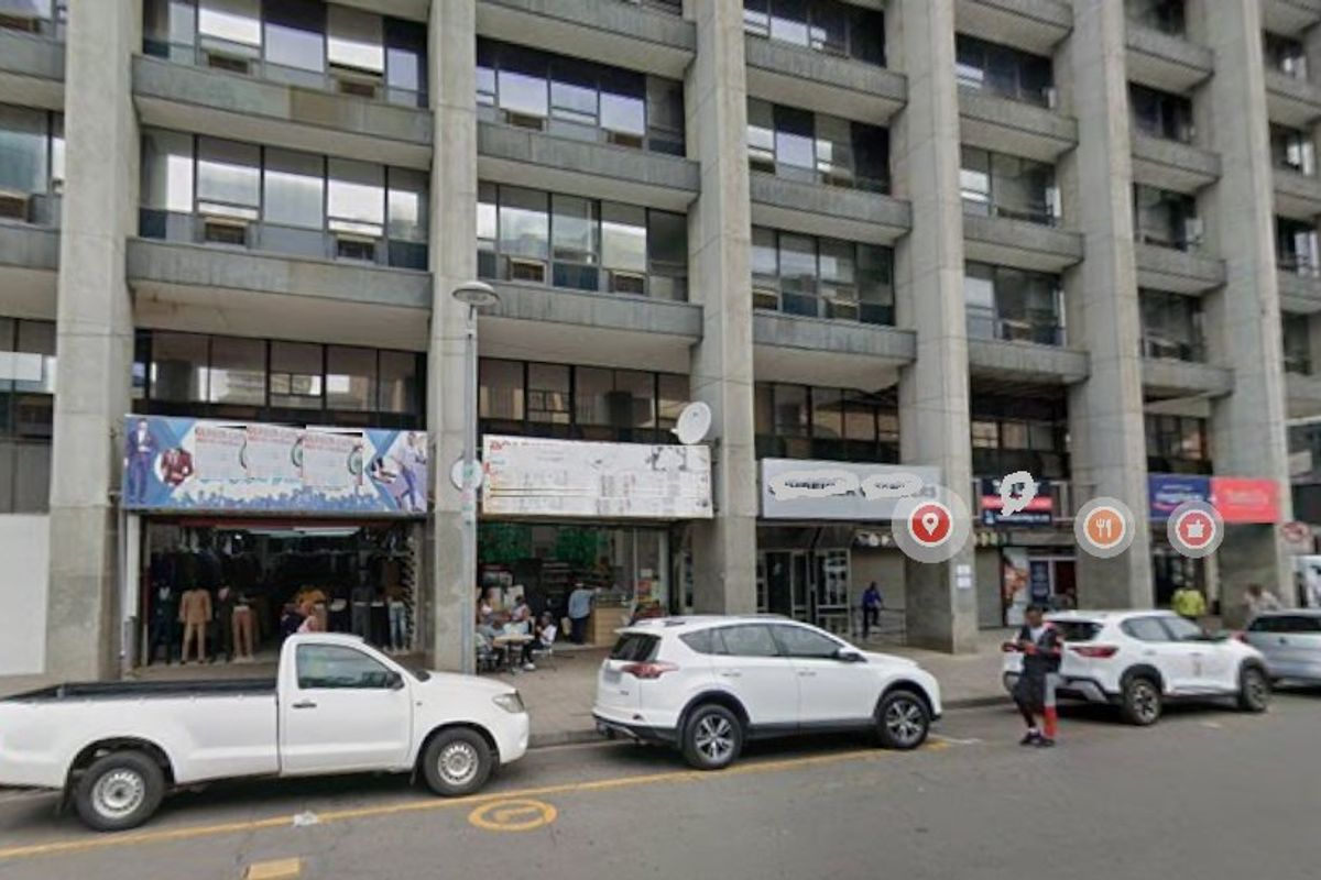 Street-level view of a multi-story commercial building featuring concrete structural elements and multiple ground-floor retail storefronts.